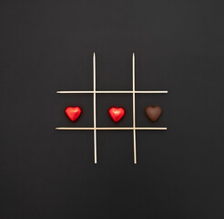 Happy Valentine's Day.  Game of tic-tac-toe with chocolate hearts with and without wrapper. black...