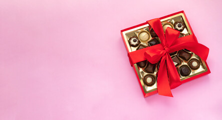 Box of chocolate pralines with red bow on pink background. Image with copy space