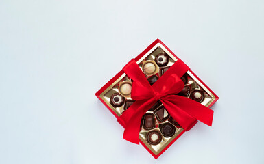 Box of chocolate pralines with red bow on light blue background. Image with copy space