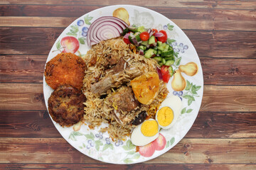 Home style mutton kacchi biryani with potato chop tomato cucumber onion salad on old style plate over rustic wood background