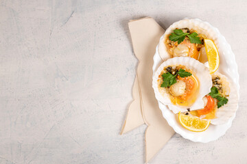 Baked scallops with caviar and creamy garlic sauce in white plate. Scallops with lemon on white background with napkin. Top view. Copy space.