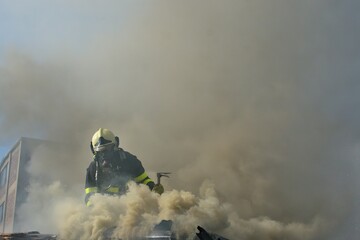 Firefighter with a crowbar hooligan tool in a breathing apparatus on a burning roof in thick...