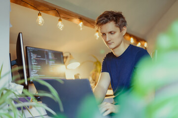 A man sitting at a desk working from home on his computer. IT specialist programmer writing code on...