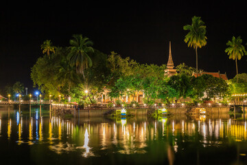 Fototapeta na wymiar Pagoda and monastery complex Wat Traphang Thong temple during night with wooden bridge and reflection, Sukhothai, Thailand