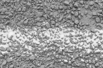 Texture of dark gray building facade cement plaster with fine gravel and stuck snow. Grey stone wall. Cheap finishing of facade of building with raw fine stone and plaster.
