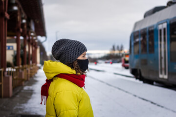 Woman wearing protective face mask and traveling by train during covid-19 pandemic. Public transportation in winter