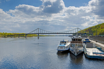 Fototapeta premium Footbridge Dnipro river panorama embankment with tourist boats Kyiv Ukraine