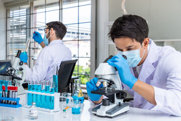 Two male Asian and Arab researcher scientists working in laboratory, conducting study biohazard substance with scientific equipment and microscope