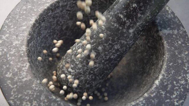 Super close-up of the white peppercorns falling into the grey stone mortar in slow motion