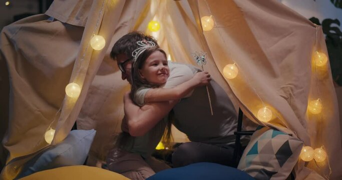 Happy father and little daughter embracing and playing in kids tent