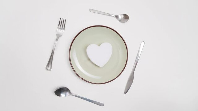 Romantic valentines day dinner idea concept. Heart on plate and silver wear on white background. Stop motion animation.