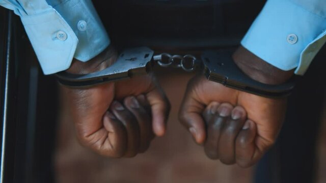 Close up of afro-american criminal in handcuffs shaking hands trying to free