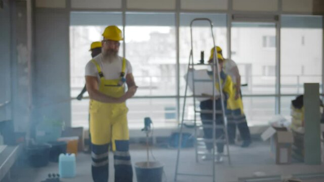 Portrait of bearded senior builder in safety overall and hardhat at construction site