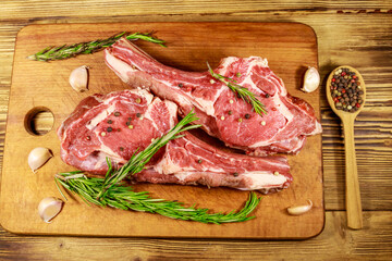Raw fresh beef rib eye steak on bone with spices, garlic and rosemary on wooden table. Top view