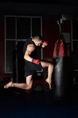 Fotobehang Kickboxing fighter Performing Jumping Air Kicks with Knee on Punch Bag. Caucasian Man Practicing Martial Arts Training at Urban Gym. High quality photo. © herraez