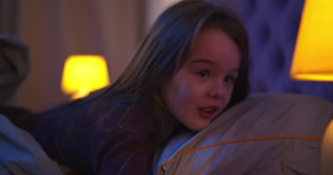 Side view of beautiful little girl turning off night lamp and falling asleep