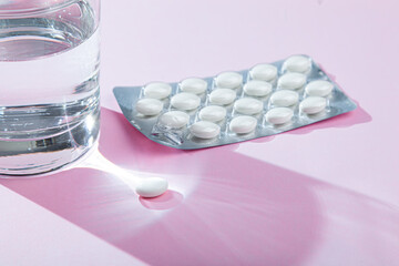 Water glass, blister with medical pills, tablets, vitamins on pink background