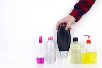 Isolated bottles of detergents on a white background. The hand takes the jars of detergents. In the photo, shampoo, micellar water, liquid soap and mouthwash. Household chemicals in colored containers