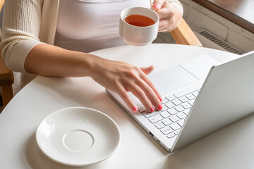 Lonely woman freelancer enjoying having breakfast with cup of coffee working on laptop sitting near window in cafe at morning. View on bust of female