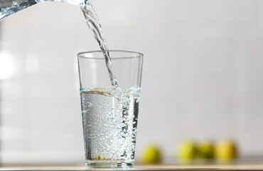 Glass of water is poured from the jug into a glass in a kitchen table