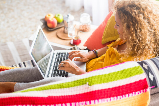Adult young woman at home use laptop computer lay down on the sofa - image of people and home work job technology with internet connection - happy free people in alternative office smart working