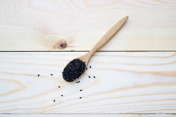 Black sesame seeds in wooden spoon pile on wood table