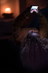 Woman at home use the internet web mobile phone lahying on the sofa by night - female people laying on the sofa enjoying the cellphone alone chatting and messaging - people and connection