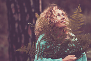 Portrait of happy cheerful woman holding big leaf in the forest with trees in background - concept of nature protection and save planet earth from deforestation - nature outdoor respect