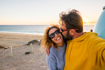Happy couple take selfie picture at the beach with love and kiss - concept of people tourists enjoy the outdoor leisure activity in travel summer holiday vacation with sky and sunrise ocean view