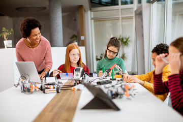 Happy kids with their African American female science teacher with laptop programming electric toys and robots at robotics classroom