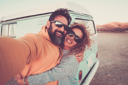 Love and happiness lifestyle with young adult pretty couple take selfie picture outdoor with vintage van vehicle in background - travel and adventure alternative free vacation
