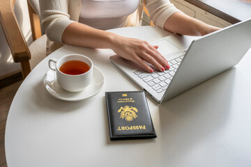 Woman tourist having breakfast with cup of coffee putting american passport on the table sitting near window in cafe in airport. Travel concept