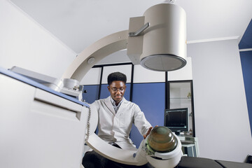 Bottom view of young confident African doctor in white uniform, working with modern lithotripter...