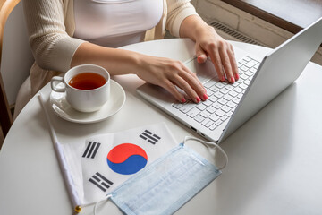 Woman tourist having breakfast with cup of coffee working on laptop.  Flag of South Korea, medical protective face mask on table of cafe. Protection from bacteria and viruse in a public place.
