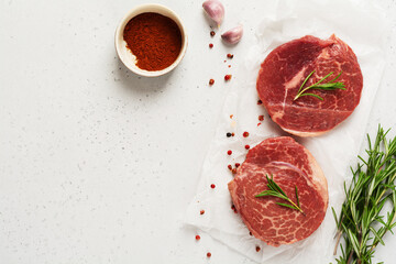 Two fresh Parisienne raw steak on white parchment paper with salt, pepper and rosmary in a rustic style on old wooden background. Black angus. Top view.
