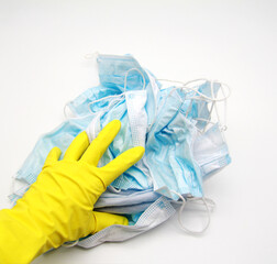 A woman's hand in a yellow glove cleans up a lot of discarded used medical masks.Infectious waste is prevented by the covid-19 virus, a pandemic.The concept of improper disposal is dangerous.