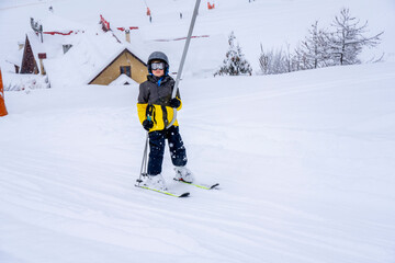 Blurred focus background. A boy lifting on the ski drag lift rope in bright sport outfit on the ski resort mountain do a ski lesson during a snowfall. Ski resort in french mountains.