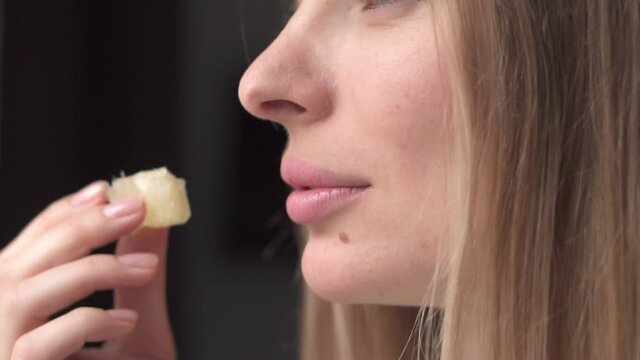 Woman eating juicy slice of pomelo at kitchen, close up portrait