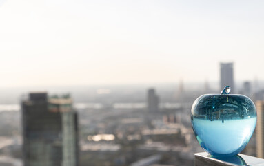 Glass or Crystal blue apple and reflective surface on cityscape background. Selective focus.