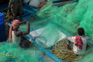 Some fishermen repairing their fishing net before going to sea for fishing.