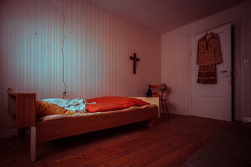 Old bedroom with cross and chair in an abandoned building with natural decay