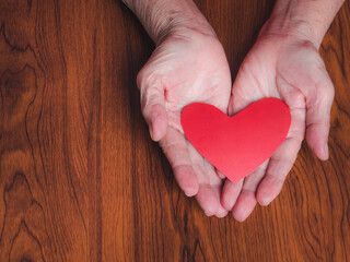 Fototapeta premium Red paper cut a heart shape on the palm of a senior woman. Valentine's day. Close-up photo. Concept of aged people and love