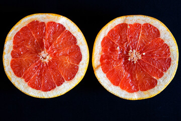 Two halves of a cut fresh red juicy grapefruit lie on a black surface. View from above. Healthy...