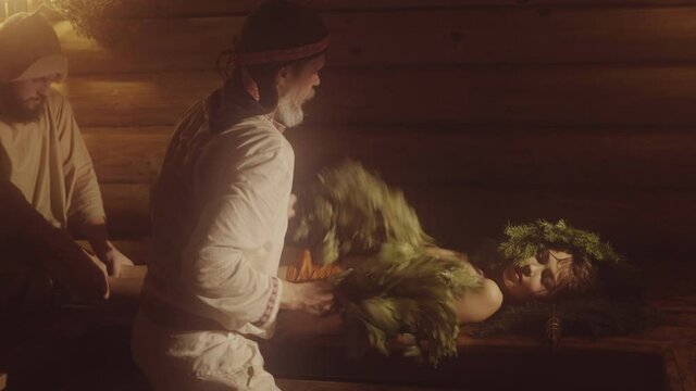 Two Bath Attendants Are Making Massage With Oak Brooms To A Boy In Sauna
