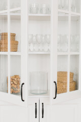 Opened white glass cabinet with clean dishes and decor. Organization of storage in kitchen.