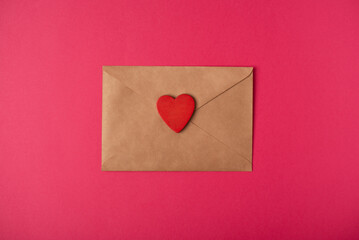 Craft envelope with the red wooden heart  on the hot pink background. Flat lay, top view. Romantic love letter for Valentine's day concept.