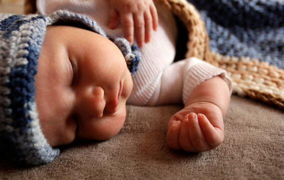 Sweet infant newborn baby boy with chubby cheeks sleep in bed covered by plaid in warm blue knitted hat during day