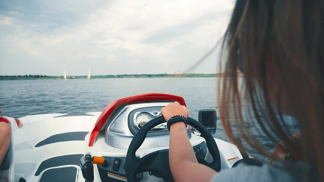 Steering wheel of a moving boat is being held by a person. Long haired woman holding her hands at the steering wheel and leads of the yacht while spending time at the open sea or ocean. Trip concept