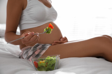 Obraz na płótnie Canvas Young pregnant woman with bowl of vegetable salad in bedroom, closeup. Taking care of baby health