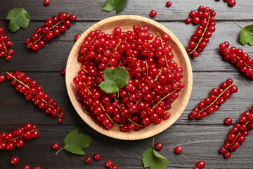 Delicious red currants and leaves on dark wooden table, flat lay